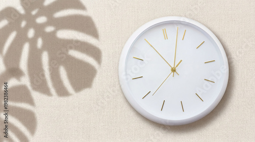 Minimalist wall clock with golden hands and tropical leaf shadows on textured beige background