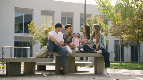 Photos Group of young college students sitting on a bench outside university building,