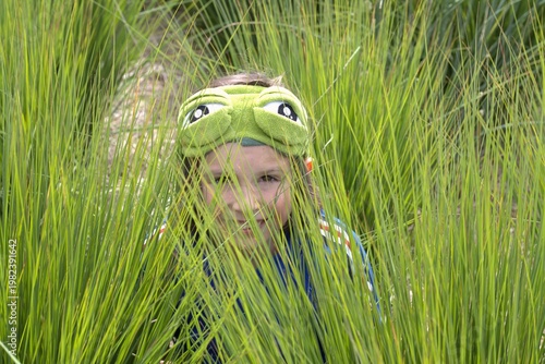 A boy in frog mask hiding in the grass