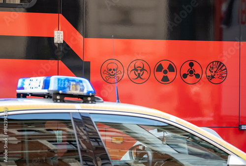 Police car beside a hazardous materials emergency response vehicle with biohazard, radiation and toxic warning symbols close-up of public safety CBRN incident containment and crisis response no people