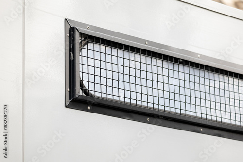 Close-up of a reinforced vehicle window with protective metal mesh grille on a white armored transport body panel angled exterior detail suggesting secure law enforcement detention transport no people