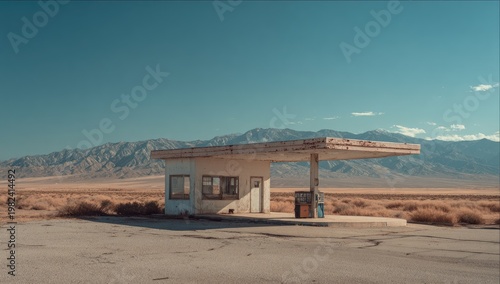 A weathered, abandoned gas station stands solitary against a vast desert landscape, framed by distant mountains under a clear blue sky.