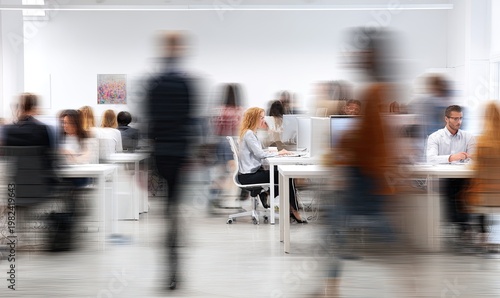 A blurred motion shot captures a bustling office environment with numerous employees working at their desks, conveying a sense of activity and productivity.
