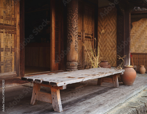 Empty Rustic Wooden Bench Outside Traditional NTT Indonesian House with Carved Column and Clay Pots, Peaceful Afternoon Light and Woven Bamboo Wall