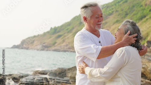 Asian senior couple embracing on seaside cliff, elderly enjoying romantic moment together, happy retirement lifestyle, love and relationship in old age, travel nature outdoor activity by the ocean