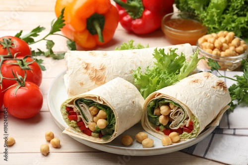 Pieces of tasty wrap with chickpeas and vegetables on white wooden table, closeup