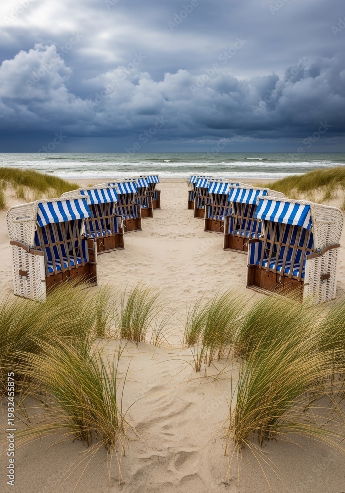 Fototapeta premium Beach chairs on sandy dune. Coastal landscape with overcast sky, ocean waves. Northern sea vacation, stormy weather concept.