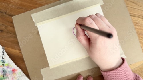 Female Caucasian hand painting a purple circle on dry watercolor paper, demonstrating wet-on-dry technique with clean edges. Close up 4K painting process on taped paper.