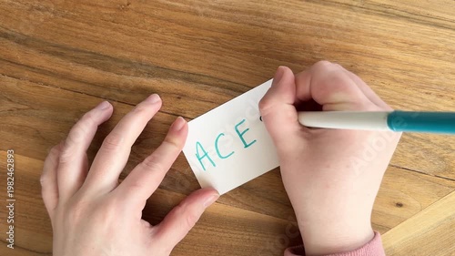 Female Caucasian hands writing “ACEO – Art Cards, Editions and Originals” on a small 2.5 x 3.5 inch card with marker. Close. up 4K lettering process on wooden table.