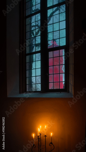 On a gloomy, rainy day, through the window of a candlelit church, could see a red Christmas building outside.