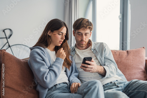 Foto A young couple relaxes on a sofa at home, intently looking at a smartphone scree