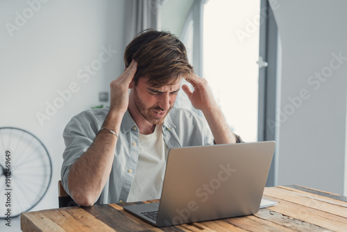 Tableau sur toile Young man experiencing frustration and headache while working on a laptop at a r