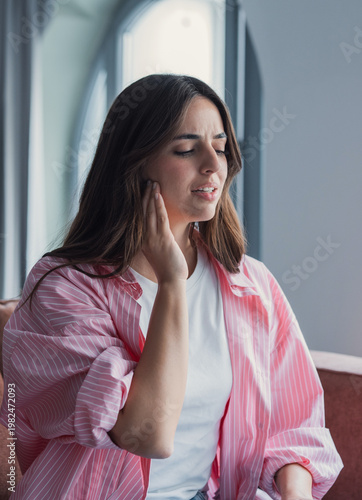 Foto A young woman sits in a bright home interior, touching her jaw with a pained expression