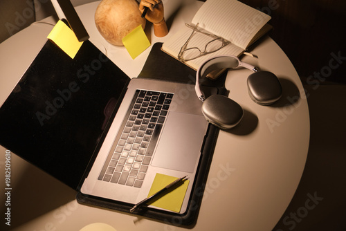 Study area with laptop, headphones, glasses, and notebook on a white table