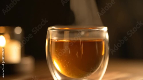 Hot steaming tea in glass cup with candle in background