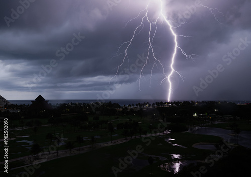 A captivating view of multiple lightning strikes hitting a scenic landscape at night, highlighting the stark contrast and beauty of stormy weather over a resort environment.