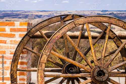 Wallpaper Mural Old wooden wagon wheels resting beside a brick wall in a rural Brazilian landscape. The image evokes a historical period when animal-drawn transport was essential for moving goods and people, Torontodigital.ca