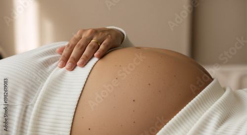 Close up of a pregnant woman touching her bare belly. Expecting mother with hand on stomach wearing a white sweater. Maternity and motherhood concept