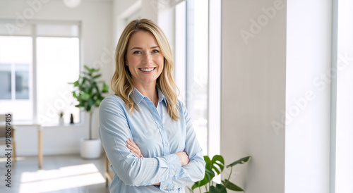 Smiling blonde businesswoman with crossed arms in a bright modern office. Portrait of a confident female corporate manager