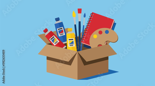 Art Supplies in Open Cardboard Box with Paints Brushes Notebook and Palette