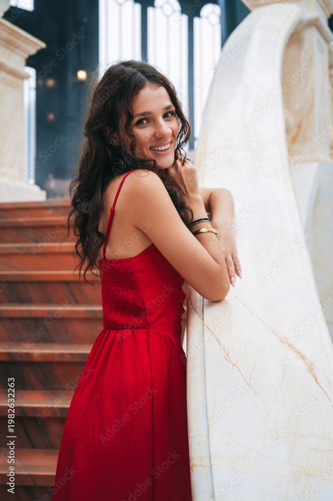 Fototapeta premium A romantic princess stands gracefully in a red dress inside an ancient castle.