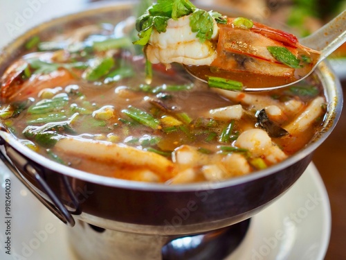 фотографія Tom Yum seafood soup with shrimp, squid, clams, fish, and mushrooms is served in a hot pot on the dining table