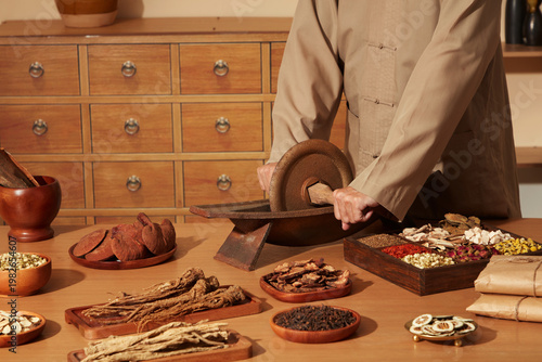 Canvastavla Hands selecting and sorting dried medicinal herbs arranged on wooden trays in traditional herbal medicine apothecary