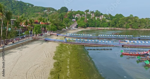 Aerial top down view of green algae spreading across the sandy shoreline of Patong Beach, Phuket. with a tractor actively cleaning the coast. The environmental maintenance, coastal ecosystem changes