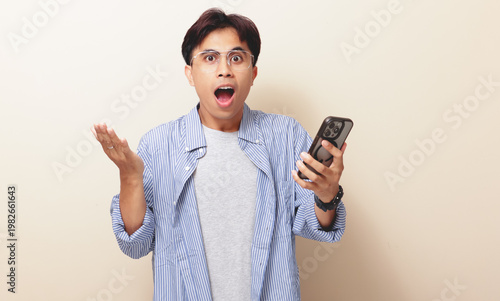 Bild auf Leinwand Wow face of a shocked Asian man looking at his smartphone with an amazed expression, isolated background