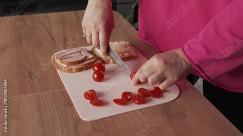 A housewife slices tomatoes to make sandwiches. Delicious breakfast at home.