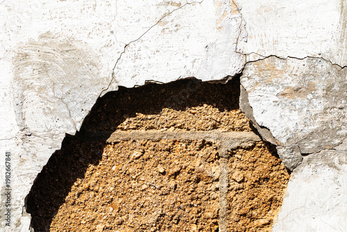 weathered white plaster wall with a large hole exposing inner brickwork