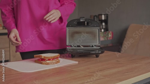 A housewife puts an electric mini grill for making sandwiches on the table.
