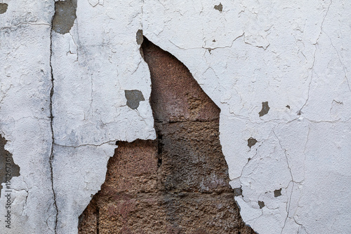 weathered white plaster wall with a large crack exposing inner brickwork