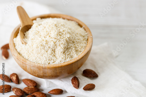 Almond meal, Almond flour, in wooden bowl with almond nuts on white table.