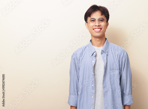 Bild auf Leinwand Smiling confident young Asian man standing and looking at camera on isolated background