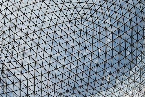 Close-up view of a geodesic glass dome roof with triangular glass panels and steel frames. The architectural structure shows a geometric pattern against the sky seen through those glass window panels