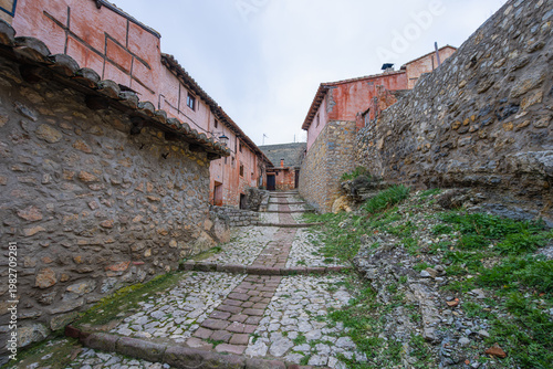 A narrow cobblestone street lined with historic red stone buildings in the medieval town of Albarracin, Spain, a beautiful village.
