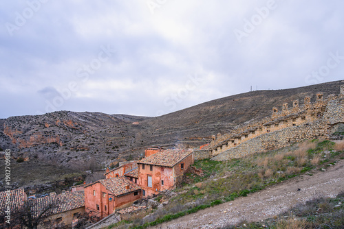 A scenic view of the historic medieval village of Albarracin in Spain, featuring ancient stone walls and traditional orange-tiled houses on a hillside.