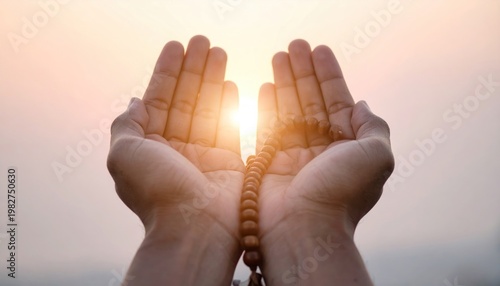 Hands holding prayer beads with sun shining through.