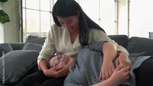 Mother gently holding and comforting her daughter with Down syndrome lying on sofa, showing love, care and family support at home
