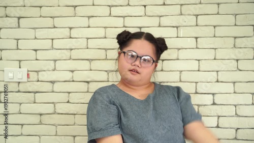 Young woman with Down syndrome stretching arms and smiling in front of brick wall, representing health, wellbeing and positive lifestyle
