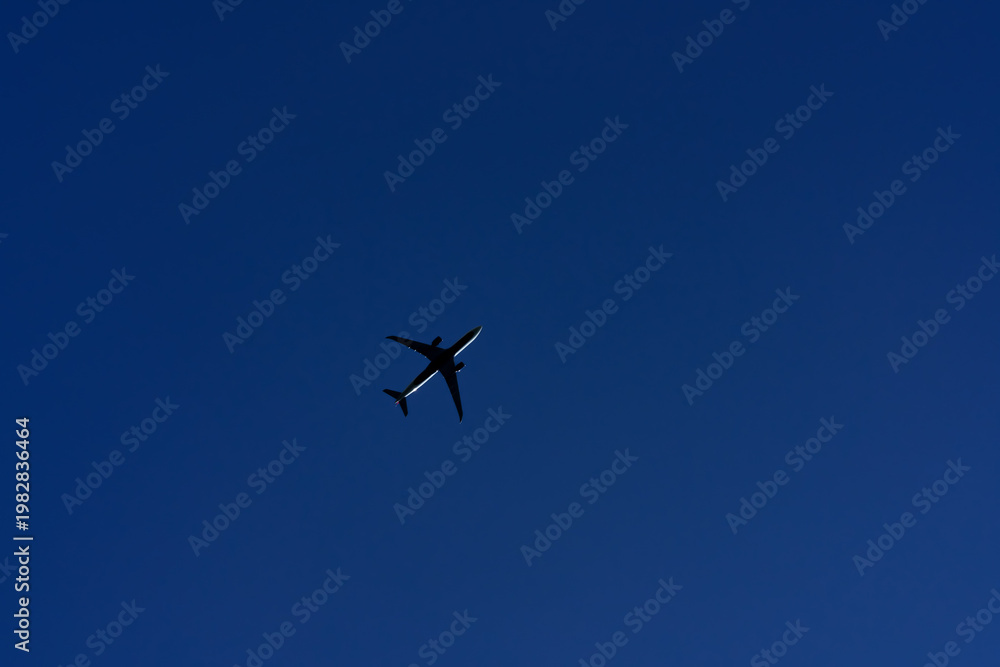 Fototapeta premium Passenger airplane flying overhead against deep blue sky, minimal composition in spring or summer with sense of freedom and motion.