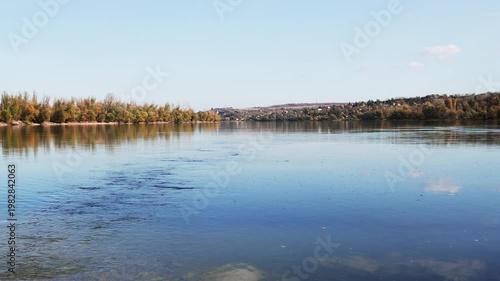 Cinematic tranquil shot of a wide river on a warm summer day. Calm water, soft sunlight, and peaceful natural scenery create a relaxing, atmospheric landscape.
