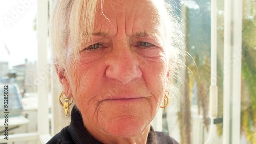 Close-up portrait of a serious senior woman with deep wrinkles and expressive eyes. Natural light highlights her face and golden hoop earrings