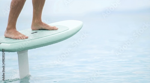 E-foil surfboard with rider standing on the water, showcasing high-tech design and hydrofoil technology in a serene aquatic environment