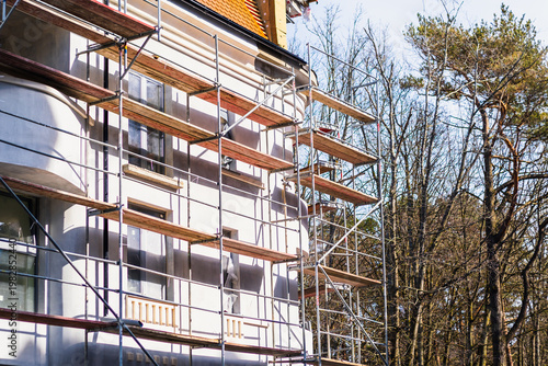 Metal scaffolding installed on gray building facade under renovation. Exterior construction work and house maintenance concept. Industrial structure for repair or plastering project.