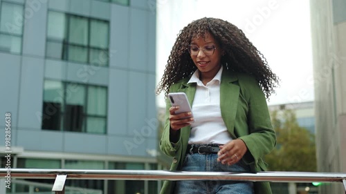 Young African American business woman using mobile phone app standing in corporate urban district. Inspired creative female professional in the city 