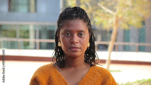 A poised young woman with intricate braided hair stands confidently, exuding a sense of strength and determination. Her expression reflects a moment of introspection and self-assuredness.