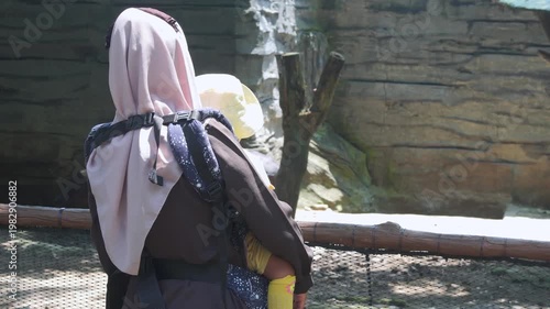 Woman at a zoo with child, observing animals behind a fence. Perfect for illustrating family outings, wildlife conservation, and education.