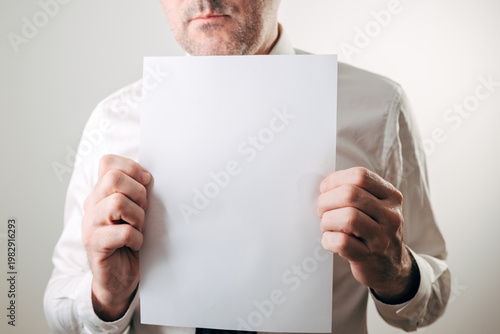 Businessman holding a blank white paper sheet, mockup for notices, contracts, warnings, announcements and resumes